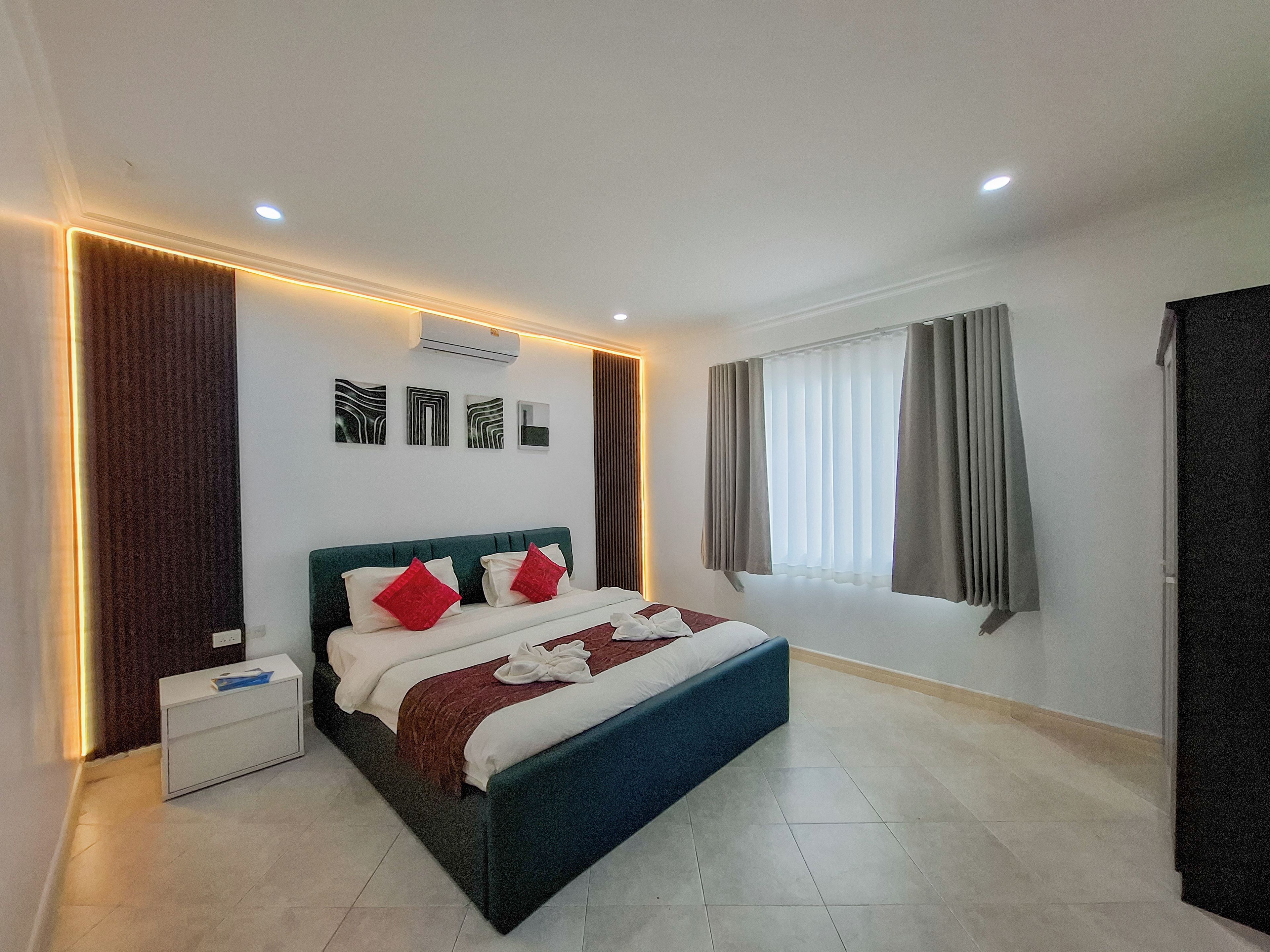 A modern hotel room with a large bed, a bedside table, a window with curtains, and wall-mounted artwork.