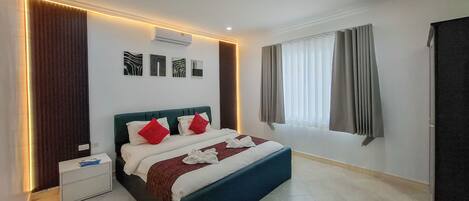 A modern hotel room with a large bed, a bedside table, a window with curtains, and wall-mounted artwork.