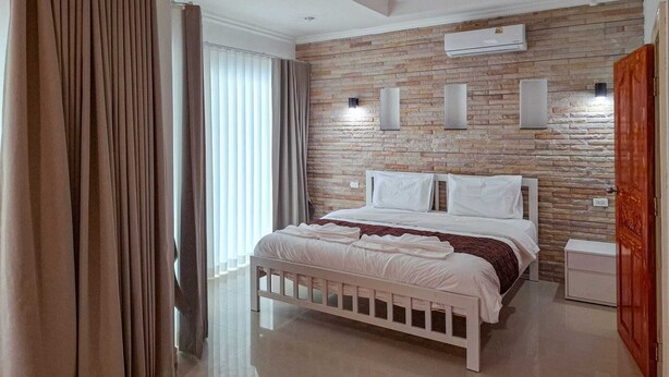 Ein modernes Schlafzimmer mit Steinwand, einem Bett mit weißer Bettwäsche und einer Klimaanlage.