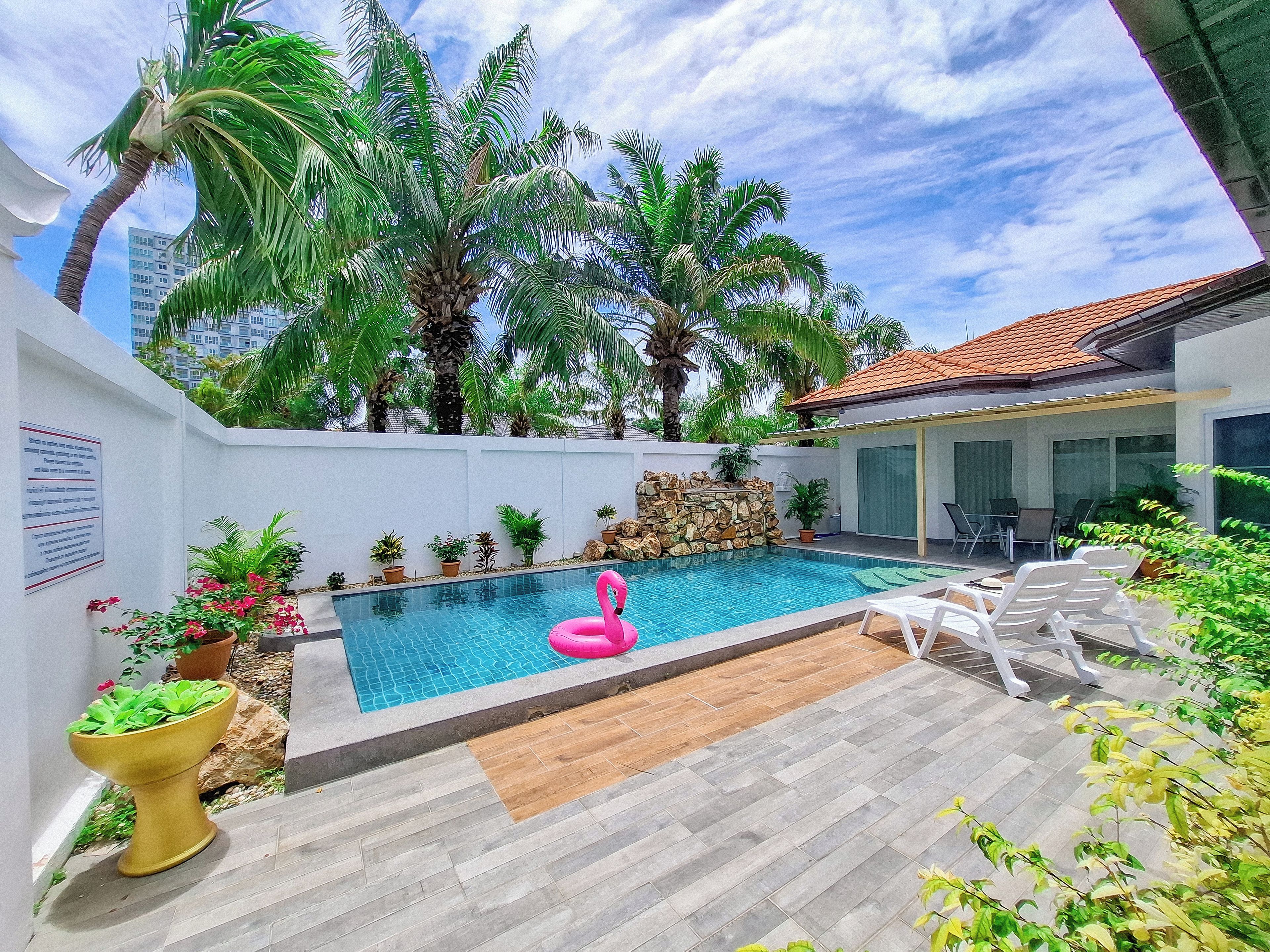 A swimming pool with a pink flamingo float, surrounded by palm trees and potted plants.