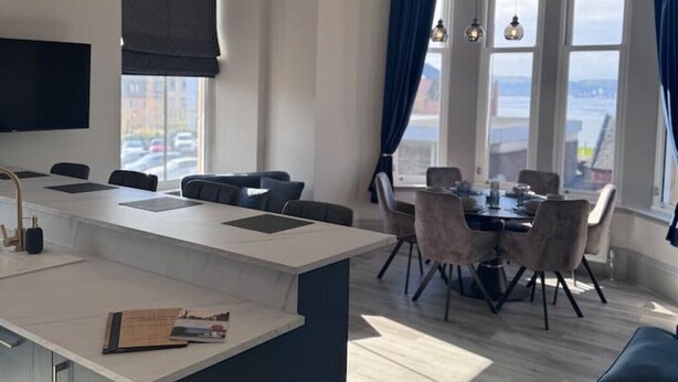 Una cucina moderna con isola centrale, zona pranzo con sedie e un'ampia finestra con tende.