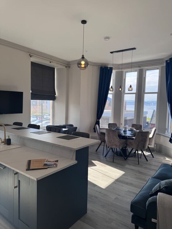 Una cocina moderna con una isla central, comedor con sillas y un amplio ventanal con cortinas.