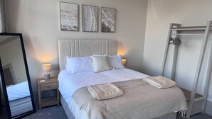 Un letto ben rifatto con una testiera, una lampada da comodino e un asciugamano piegato.