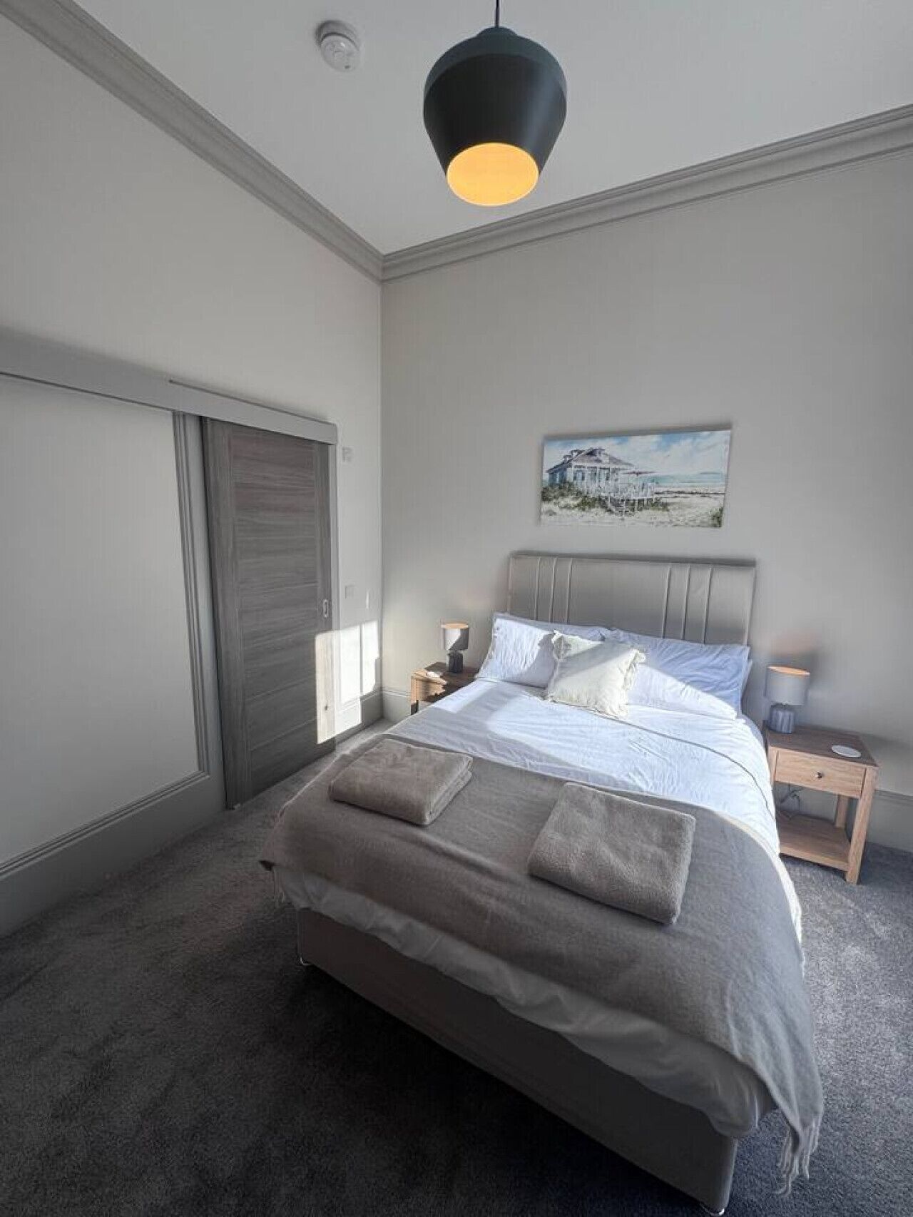 Ein Schlafzimmer mit einem Bett, Nachttischen, einem Bild an der Wand und einer Deckenleuchte.