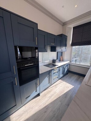 Una cocina moderna con armarios oscuros, horno empotrado y ventana con vistas.