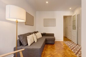 Ein modernes Wohnzimmer mit einem grauen Sofa, einer Stehlampe und einem gemusterten Teppich.