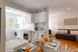 Eine moderne Küche mit weißen Schränken, ein Essbereich mit Frühstückstisch und ein Wohnzimmer mit Sofa und Lampe.