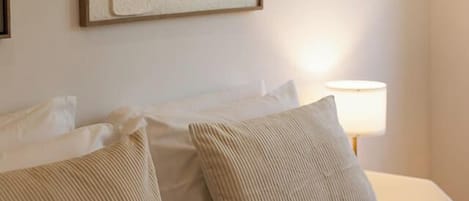Ein Hotelzimmer mit einem Bett, Kissen, einem Wandbild im abstrakten Stil und einer Nachttischlampe.
