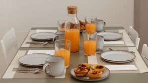 Mesa de café da manhã posta com pratos, copos, jarra de suco de laranja e garrafa de suco.