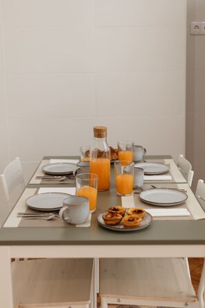 Ein Frühstückstisch gedeckt mit Tellern, Gläsern, einer Kanne Orangensaft und einer Saftflasche.