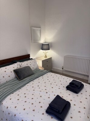 Ein Schlafzimmer mit einem Bett, einem Nachttisch mit Lampe, einem Heizkörper und einem gerahmten Bild an der Wand.