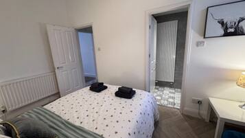 A hotel room with a bed, a desk, and a door leading to a bathroom.