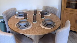 Ein runder Esstisch mit sechs Stühlen, eine Holzkommode und ein abstraktes Wandbild.