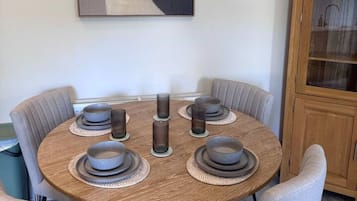 Una mesa de comedor redonda con seis sillas, un aparador de madera y un cuadro abstracto colgado en la pared.