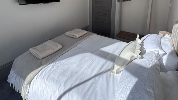 Ein Schlafzimmer mit einem Bett, einem an der Wand montierten Fernseher, einer Tür und einer Pendelleuchte.