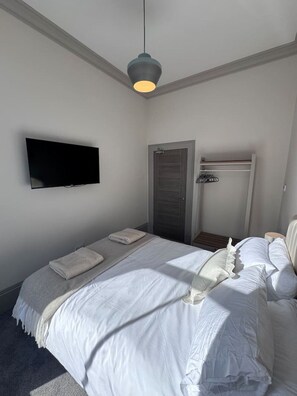 Un dormitorio con cama, televisor montado en la pared, puerta y lámpara colgante.