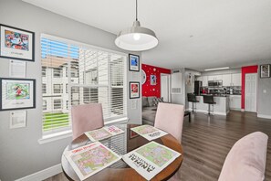 A modern kitchen with white cabinets, a red accent wall, and a dining area with a round table and pink chairs. - Red Inspired Disney Area Condo 2BR w/ Resort Pool (Kissimmee)
