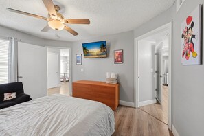 Ein Schlafzimmer mit einem Bett, einer Holzkommode, einem Deckenventilator und Kunstwerken an den Wänden.