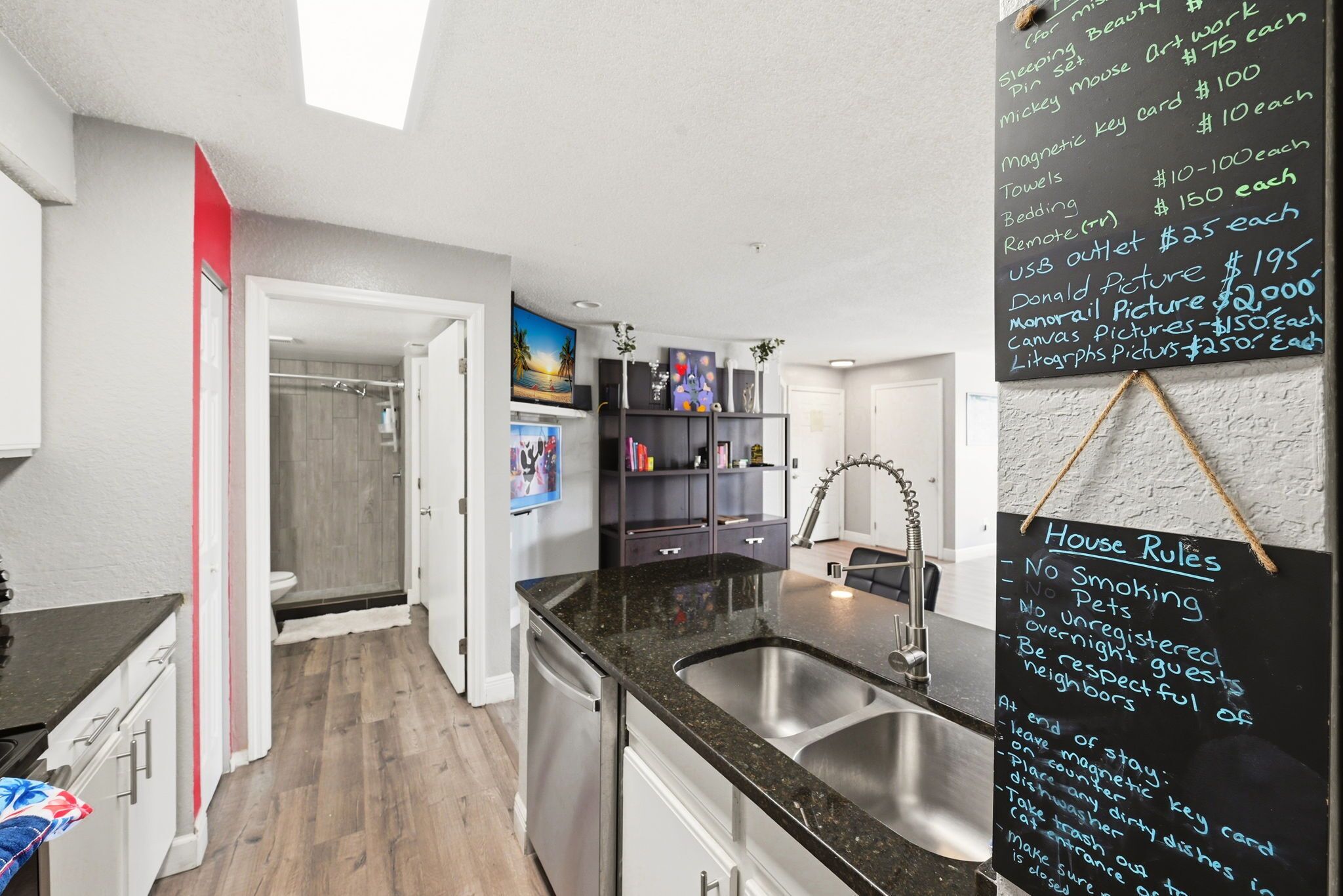 A modern kitchen with a blackboard listing amenities and prices, a sink, and a view of the adjacent bathroom.