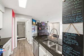 A modern kitchen with a blackboard listing amenities and prices, a sink, and a view of the adjacent bathroom. - Red Inspired Disney Area Condo 2BR w/ Resort Pool (Kissimmee)