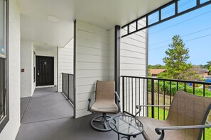 Ein Balkon mit zwei Stühlen, einem Glastisch, einer Tür und Blick auf eine Wohngegend.