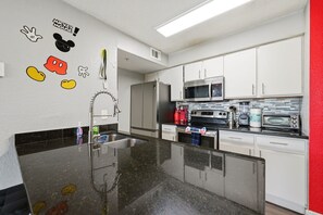 Une cuisine moderne dotée d’appareils électroménagers en acier inoxydable, d’un plan de travail en granit et d’un mur d’accent rouge.
