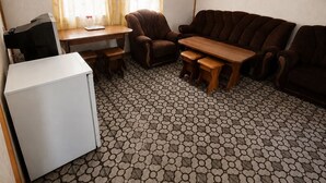 A compact living space with a sofa, armchair, and a small table. A refrigerator is against the wall, and a window with curtains is visible. - Lake Sevan Private Cottage with Yard (Shoghakat)