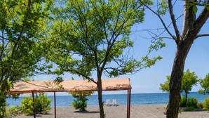 A beachside outdoor seating area with a table and chairs under a canopy, overlooking the sea. - Lake Sevan Private Cottage with Yard (Shoghakat)