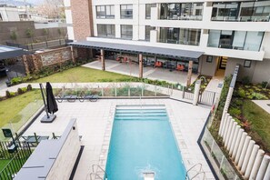 A swimming pool with a sunshade, surrounded by a garden and a building with multiple windows. - Chic Las Condes 1BR1BA Pool & Gym for 3 Guests (Las Condes)