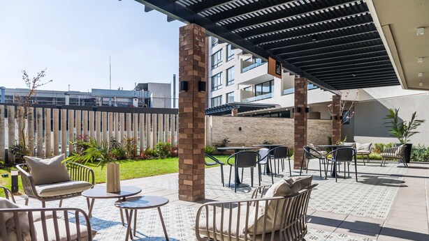 Een terras buiten met zitgedeelte, een pergola en uitzicht op de omliggende gebouwen.
