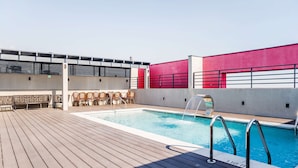 A rooftop swimming pool with a wooden deck, lounge chairs, and a red and white wall. - Beautiful 2BR Apt in Las Condes with Pool & Views (Las Condes)