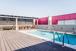 Ein Pool auf dem Dach mit Holzterrasse, Liegestühlen und einer roten und weißen Wand.