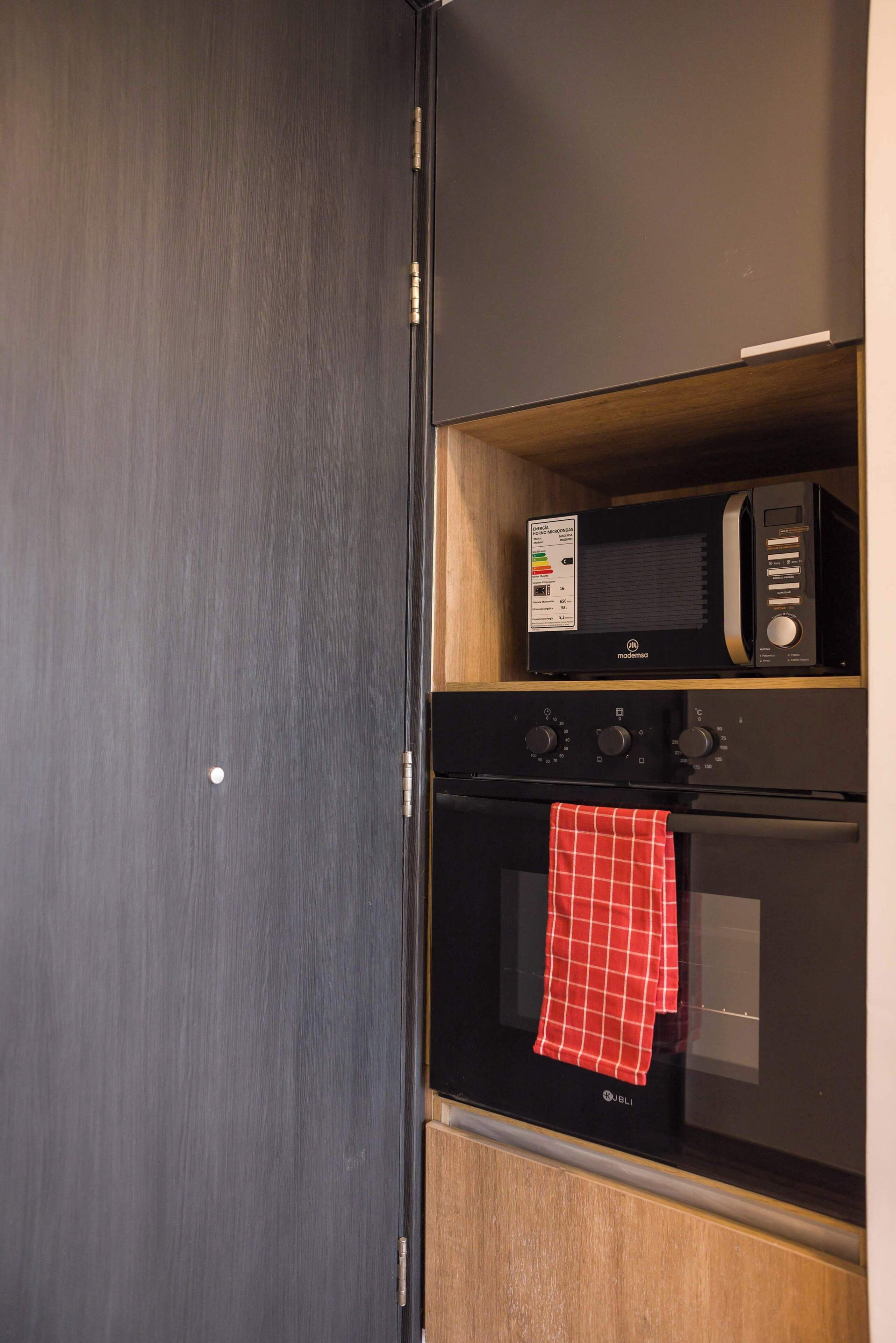 A kitchen with a microwave, oven, and a red checkered towel hanging on the oven handle.