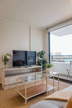A modern living room with a flat-screen TV, a glass coffee table, and two potted plants.