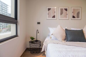 Ein Schlafzimmer mit einem Bett, einem Nachttisch mit Lampe, einer Topfpflanze und drei gerahmten Kunstwerken an der Wand.