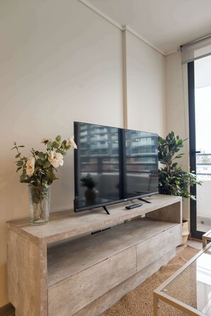Ein Flachbildfernseher an einer Holzkonsole befestigt, mit einer Fernbedienung darauf. Auf jeder Seite des Fernsehers stehen je ein Blumentopf.