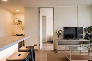 A modern living room with a flat-screen TV, a coffee table, and a seating area with stools. - Beautiful 2BR Apt in Las Condes with Pool & Views (Las Condes)