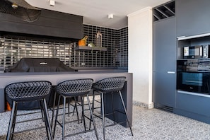 A modern kitchen with a built-in grill, bar stools, and a refrigerator.