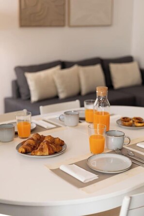 A breakfast setting with croissants, orange juice, and a bottle on a round table. - Bright, Custom-Built Apartment with Air Conditioning in Areeiro (Lisbon)