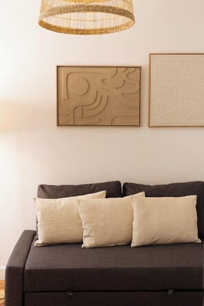 A dark-colored sofa with three beige pillows, a woven pendant light, and two wall-mounted artworks. - Bright, Custom-Built Apartment with Air Conditioning in Areeiro (Lisbon)