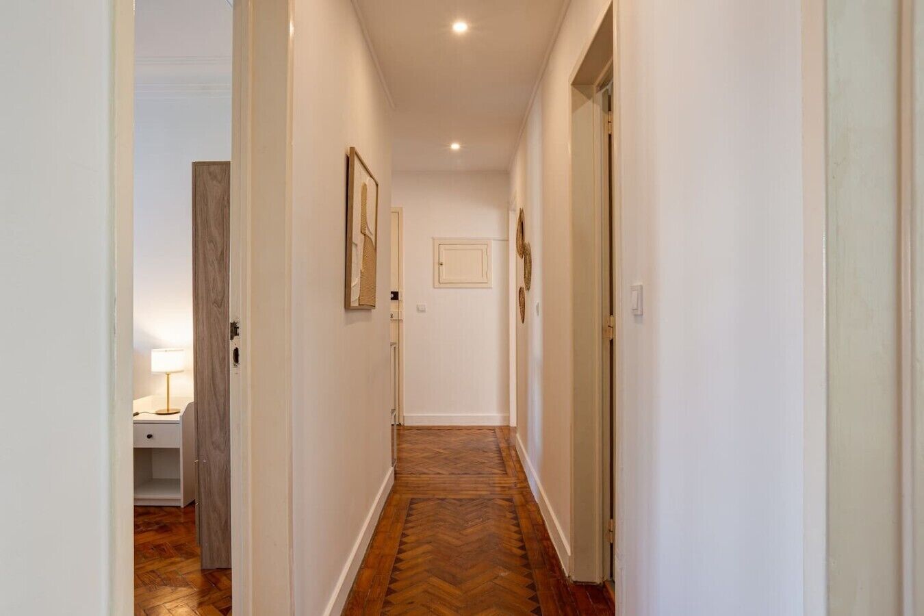 A hallway with a wooden floor, white walls, and a door at the end.