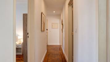 A hallway with a wooden floor, white walls, and a door at the end.