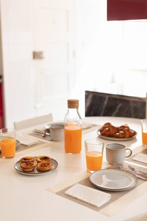 A breakfast setting with a plate of pastries, a bottle of orange juice, and glasses of orange juice on a table. - Bright, Custom-Built Apartment with Air Conditioning in Areeiro (Lisbon)