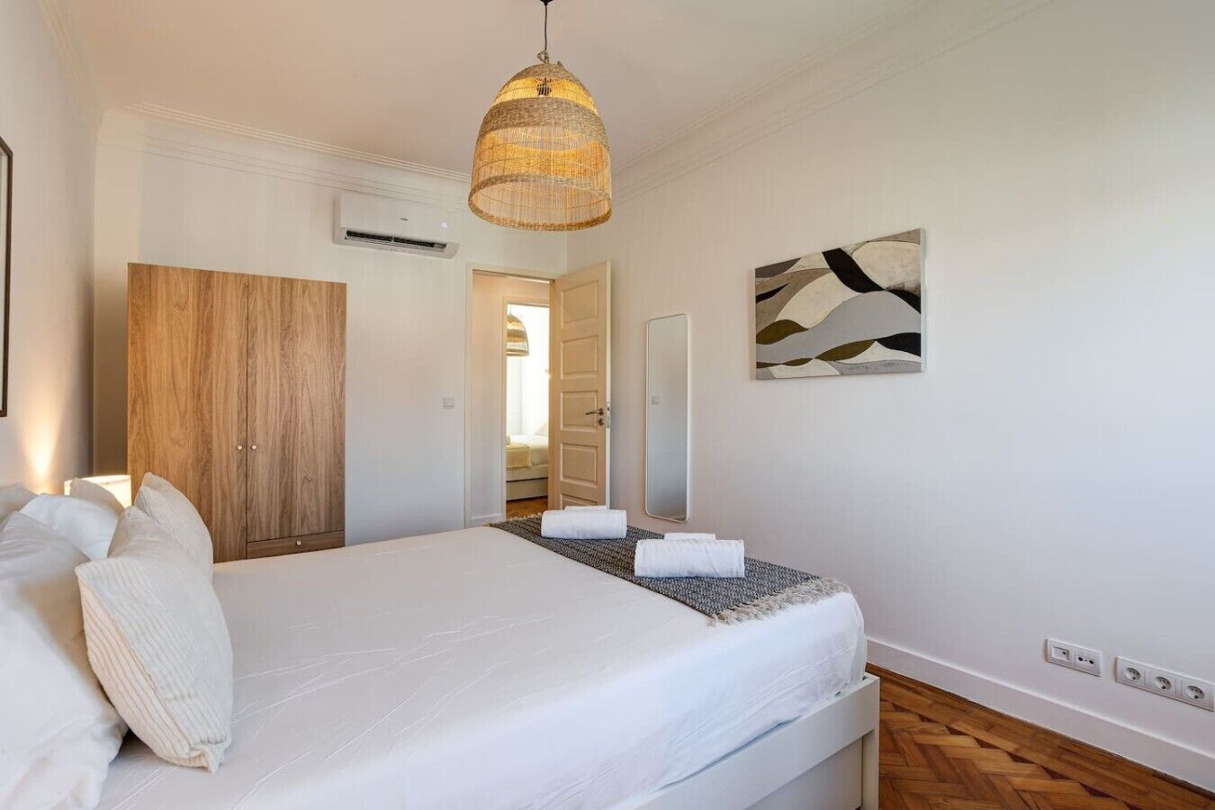 Ein Schlafzimmer mit einem Bett, einem Holzschrank, einer Pendelleuchte, einem an der Wand befestigten Spiegel und einem Gemälde.