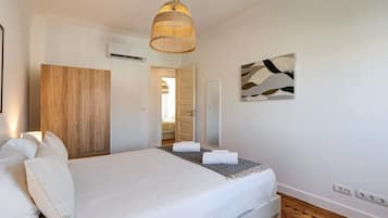 A bedroom with a bed, a wooden wardrobe, a hanging light fixture, a wall-mounted mirror, and a painting.