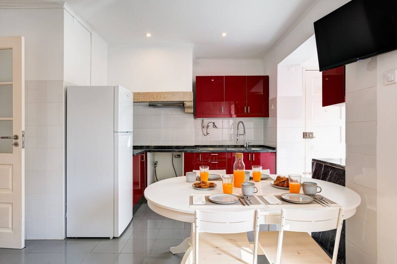 A modern kitchen with white cabinets, a red accent wall, and a dining area with a round table set for breakfast.