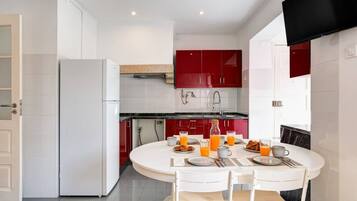 A modern kitchen with white cabinets, a red accent wall, and a dining area with a round table set for breakfast.