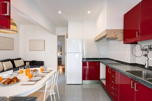 A modern kitchen with red cabinets, a white refrigerator, and a dining area with breakfast items. - Bright, Custom-Built Apartment with Air Conditioning in Areeiro (Lisbon)