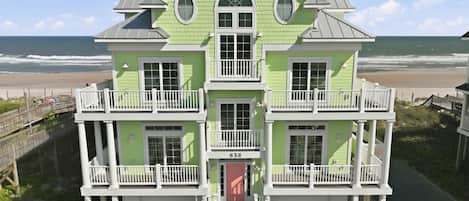 A two-story building with a balcony, a garage, and a view of the beach.
