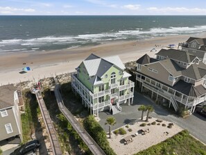 Una propiedad costera con vistas a la playa, un paseo marítimo de madera y una casa grande con varios balcones.